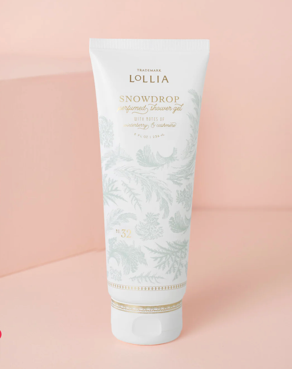Lollia Snowdrop Perfumed Shower Gel in a white satin-touch tube with sage frost botanical print and gold accent band, shown against a blush background.