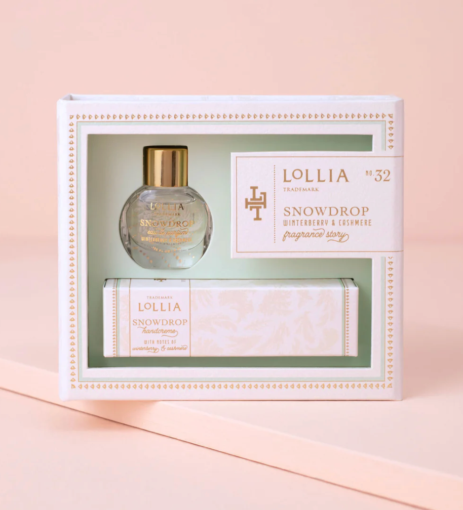 Lollia Snowdrop Fragrance Story Gift Set in a mint and white keepsake box with gold typography and border detailing, shown closed against a blush background.
