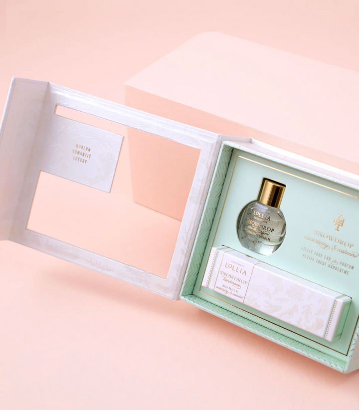Open Lollia Snowdrop gift set showing miniature Eau de Parfum bottle and Petite Treat Handcreme nestled in mint and gold interior, with book-style lid open to reveal embossed lining.