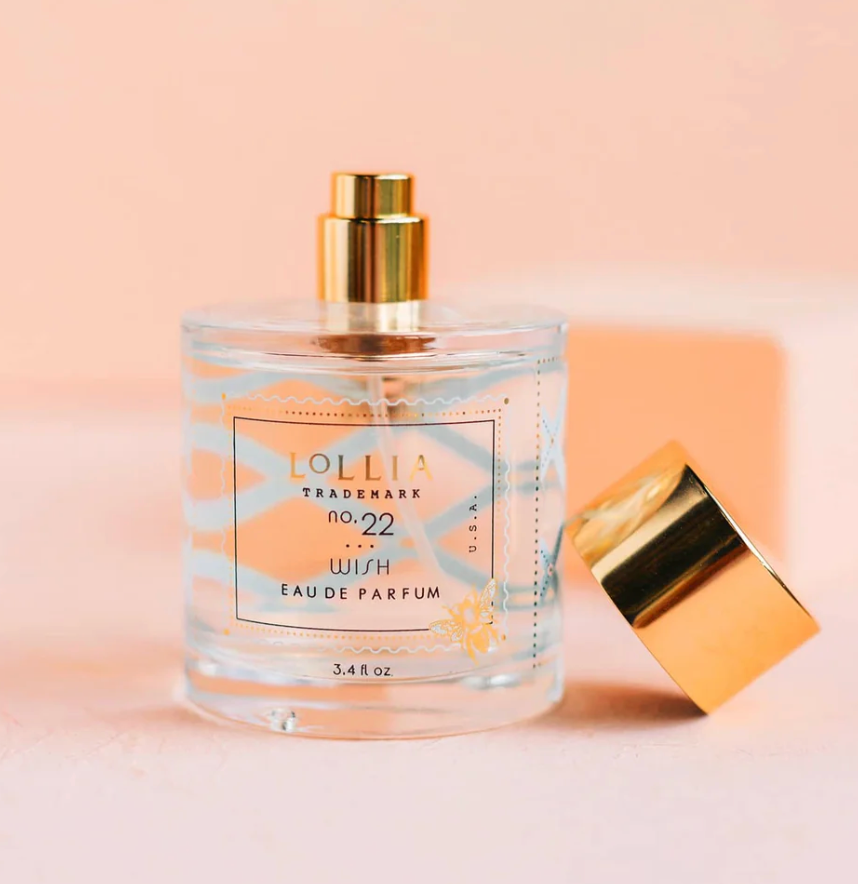 Lollia Wish Eau de Parfum in a rounded glass bottle with blue foulard print and gold bee illustration, gold pump and cap removed to the side, shown against a blush background.