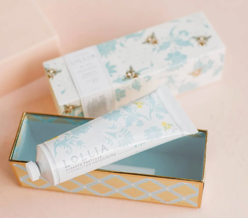 Lollia Wish Handcreme tube nestled inside open gold and aqua tray with blue lattice interior, sleeve box visible behind.