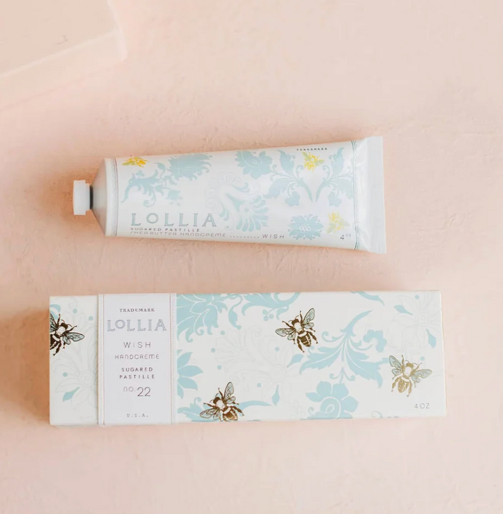 Lollia Wish Shea Butter Handcreme tube and gift box flat lay showing bee illustration and blue damask floral pattern on white ground.