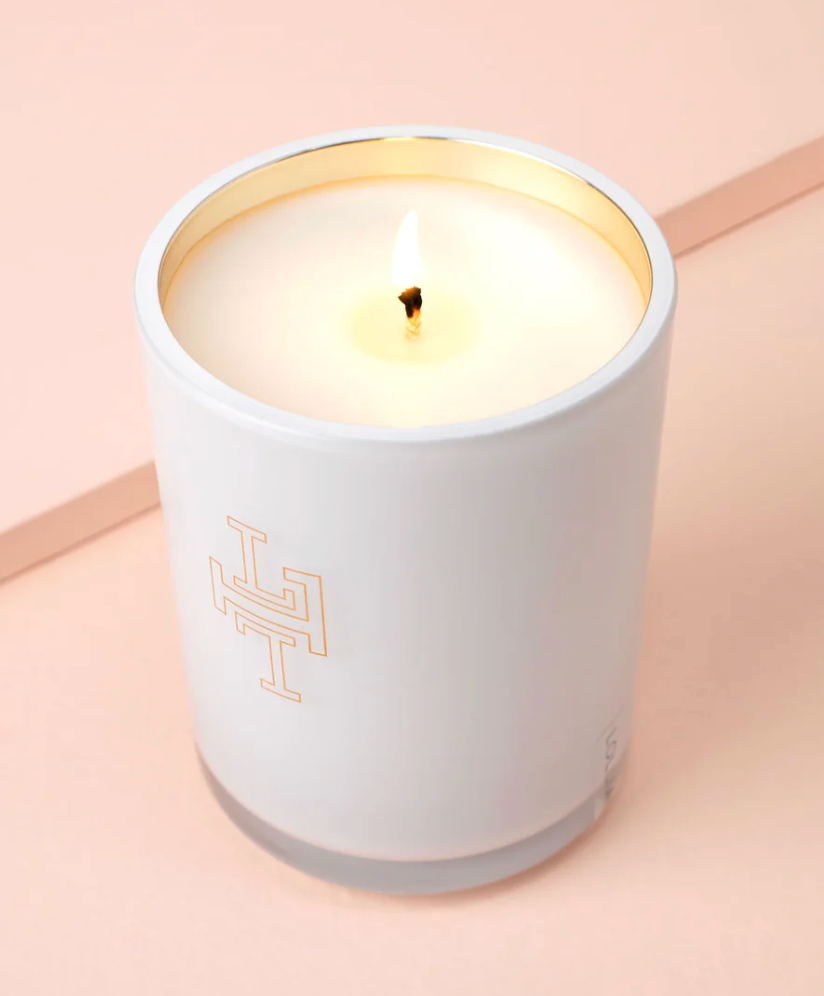 Lollia Wish candle burning in frosted white glass with gold interior rim and gold monogram detail, shown from above on a blush surface.