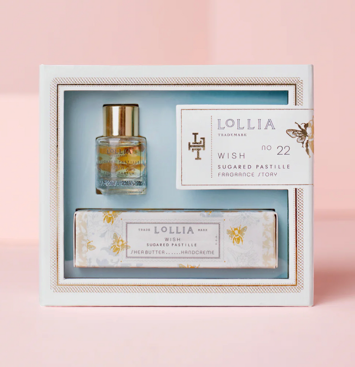 Lollia Wish Fragrance Story Gift Set in a white and blue damask keepsake box with gold bee accents and stamp-style label, shown against a blush background.