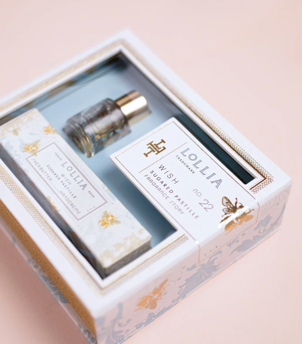 Open Lollia Wish gift set showing miniature Eau de Parfum bottle and Petite Treat Handcreme nestled in aqua interior with gold-trimmed divider and fragrance story card.