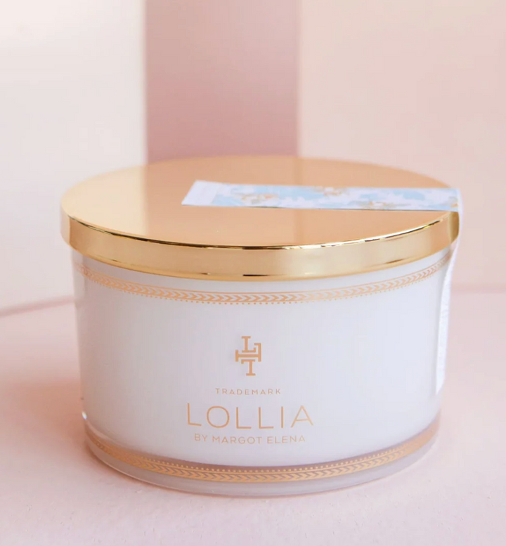 Lollia Wish Bath Salt in a white glass jar with gold accent band and reflective gold lid, shown against a blush background.