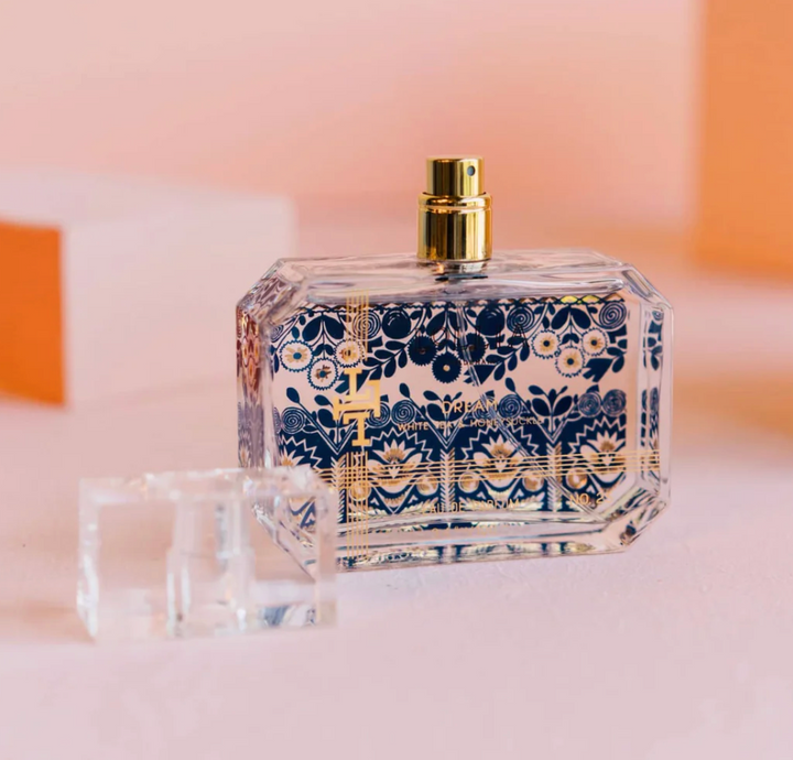 Lollia Dream Eau de Parfum bottle standing upright with clear faceted cap beside it, royal blue and gold textile-inspired print visible on all sides.