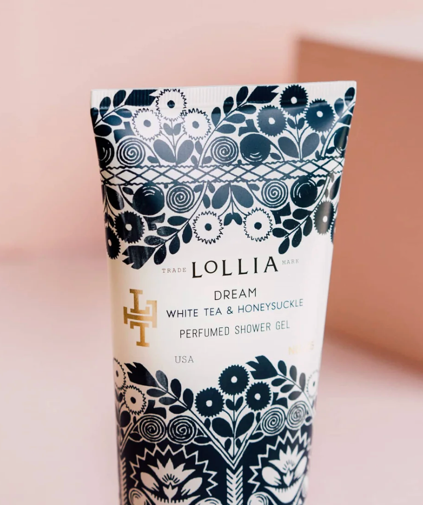 Close-up of Lollia Dream Shower Gel tube label showing navy folk-floral botanical print, gold Lollia monogram, and Dream White Tea &amp; Honeysuckle fragrance name.