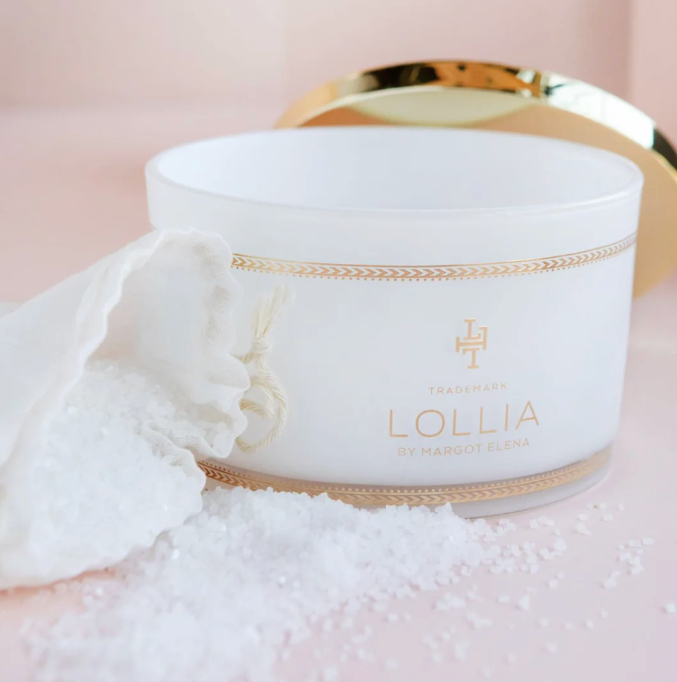 Open Lollia Dream Bath Salts jar with white linen drawstring bag and scattered sea salt crystals, gold lid and chevron banding visible.
