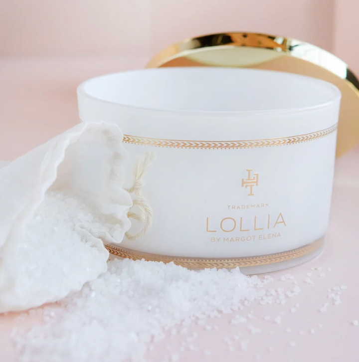 Open Lollia Dream Bath Salts jar with white linen drawstring bag and scattered sea salt crystals, gold lid and chevron banding visible.