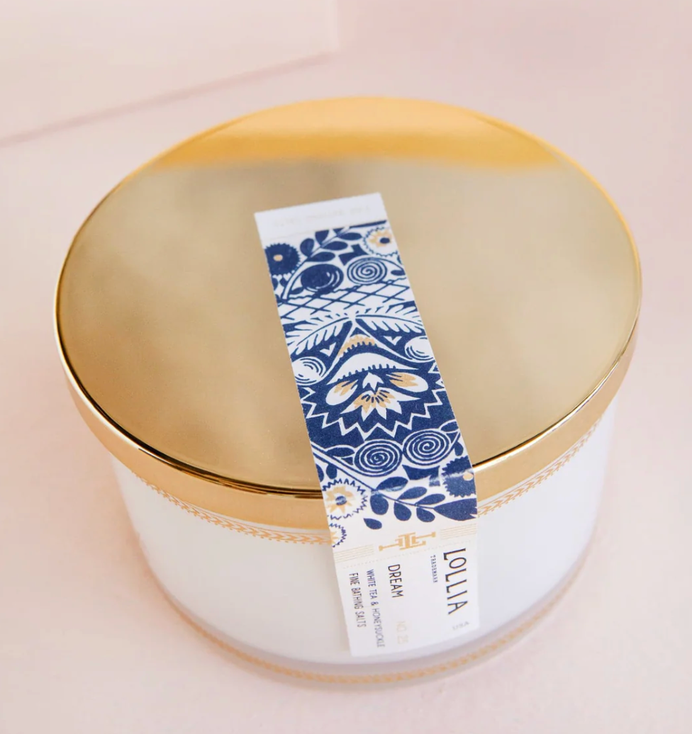 Top-down view of Lollia Dream Fine Bathing Salts gold reflective lid with navy and white folk-floral belly band crossing the surface.