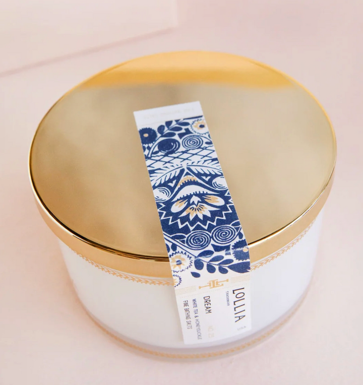Top-down view of Lollia Dream Fine Bathing Salts gold reflective lid with navy and white folk-floral belly band crossing the surface.