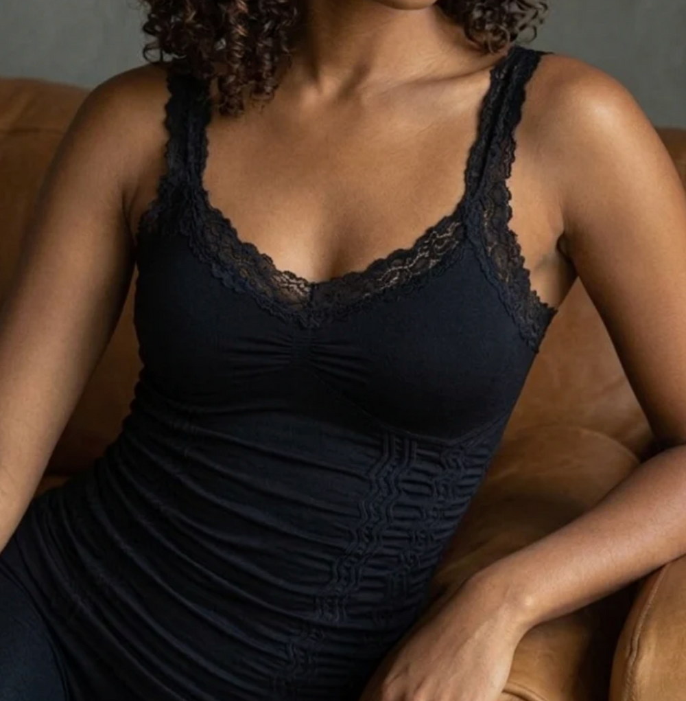 Elietian Lace Corset Cami in black with floral lace neckline trim and tonal jacquard body detail, shown seated against a warm background.