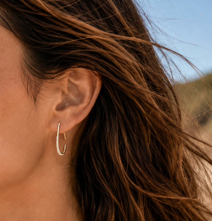 Ella Stein Drop By Anytime Hoop Earrings in gold — close-up on model showing teardrop hoop scale at ear, open frame, and diamond-set lower arc catching light.