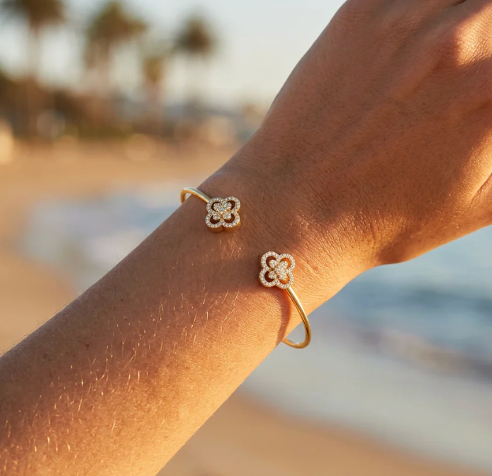 Ella Stein Wildflower Flexi Cuff Bracelet in gold — on-model wrist shot at golden hour showing both pavé clover terminals, open cuff fit, and diamond detail catching warm light.