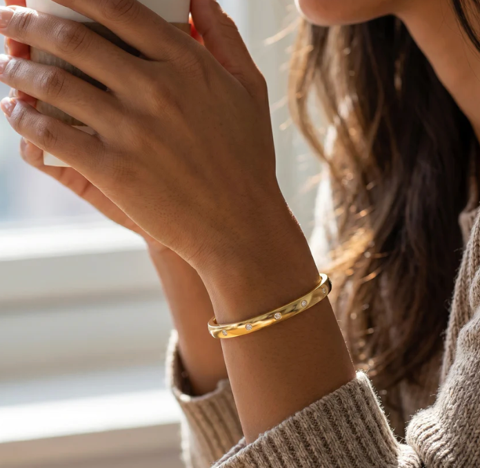 Ella Stein Lucky 7 Cuff Bracelet in gold — lifestyle wrist shot showing cuff worn against a chunky knit sleeve, bezel diamond stations catching natural light.