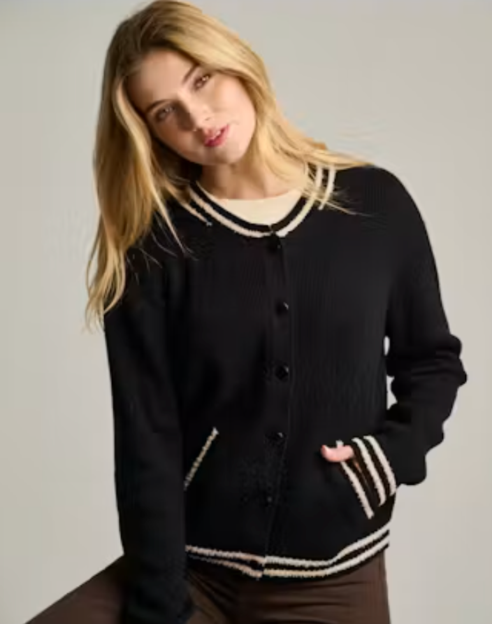 Front view of a woman wearing the Team Player Cardigan in black, a ribbed knit cardigan with contrast cream stripe trim at the collar, cuffs, pockets, and hem, worn open-front over a cream top.