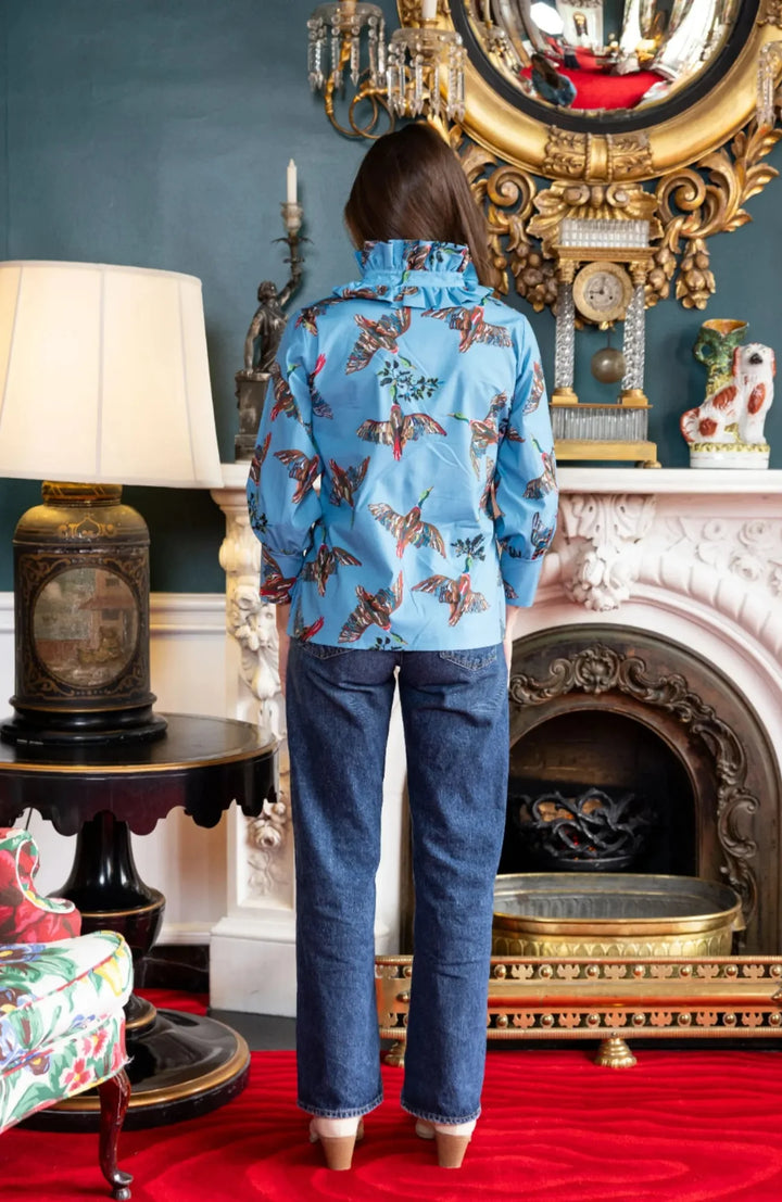 Back view, styled lifestyle: House of MBR Harper Top in Berry Grove© print shown from behind against a mantel and gilt mirror, highlighting the ruffled mandarin collar, bird print across the back, and relaxed sleeve silhouette.