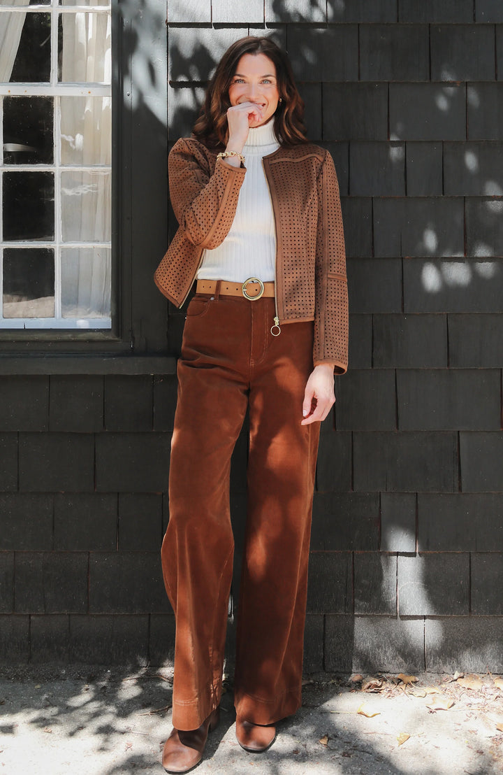 Full-length view of a model wearing the open jacket over a white turtleneck, brown corduroy wide-leg pants, and a gold buckle belt.
