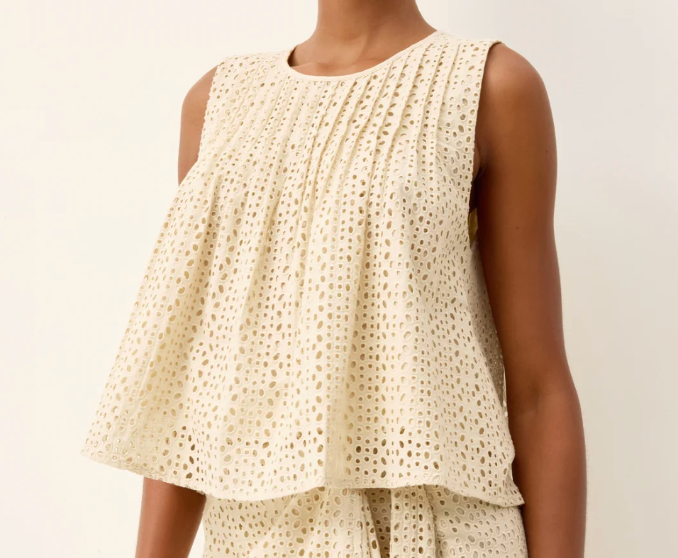 Woman wearing a cream-colored sleeveless top and skirt set against a plain background