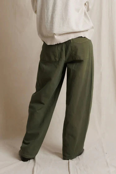 Close-up back view of a model in the dark olive utility pants, showing the back yoke and pocket detailing, paired with black shoes.