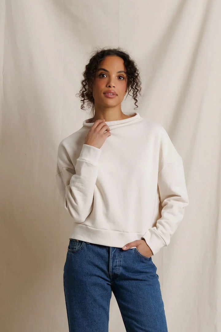 Front view, model in cream mock neck French terry sweatshirt and dark wash straight-leg jeans against a draped fabric backdrop.