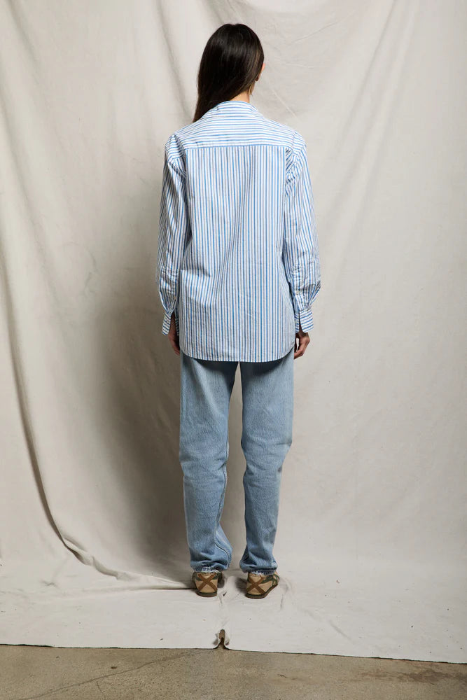 Back view of blue and white vertical stripe oversized button-down shirt showing mid-thigh length and relaxed silhouette, paired with light-wash straight-leg jeans and woven slide sandals — perfectwhitetee Avalon Cotton Poplin Shirt in Pacific Blue Stripe