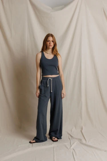 Full-length front view, model in a slate blue tank and matching French terry drawcord pants against a draped fabric backdrop.