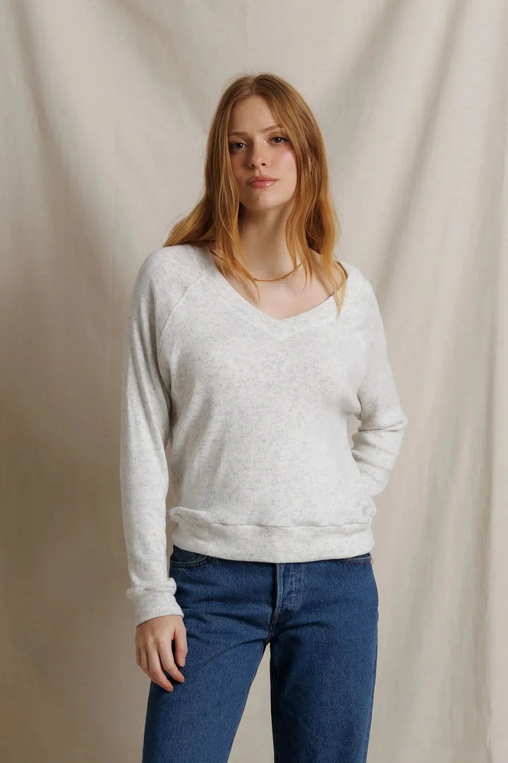 perfectwhitetee Brielle V Neck Sweatshirt in Ash, front view on model, showing a heathered light gray V-neck sweatshirt with raglan sleeves and ribbed hem, styled with medium-wash straight-leg jeans and a gold chain necklace