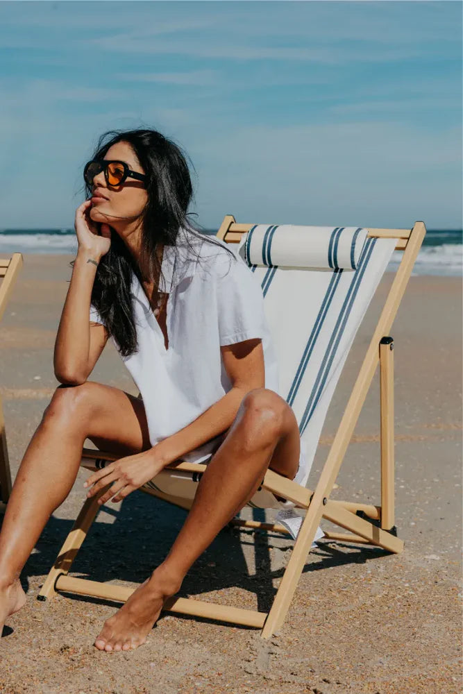 Woman in white cropped polo top seated in a beach chair on sandy shoreline, sunglasses and bare feet, ocean in background — perfectwhitetee Charlie Tennessee Jersey Polo