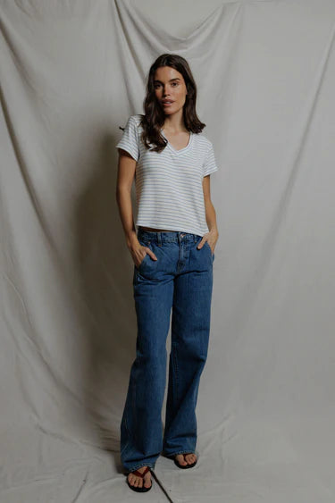 Woman wearing white and blue stripe cropped v-neck tee tucked into wide-leg blue denim jeans, styled with black flip sandals, neutral studio backdrop — perfectwhitetee Elliot Sweater Tee