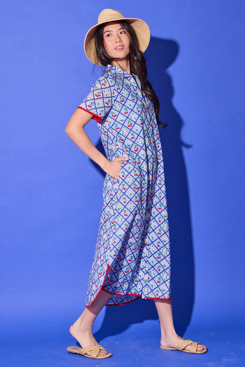 Alden Adair Josie Midi Dress, side view in light blue cherry print showing the side seam pocket, side slit at the hem, and red contrast trim.