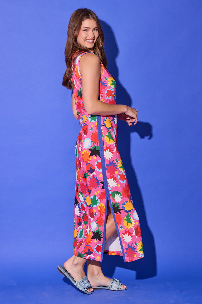Alden Adair Berkley Maxi Dress, side view in hot pink rainbow starburst print, showing the side slit with blue contrast trim, side seam pocket, and ankle-length hem.