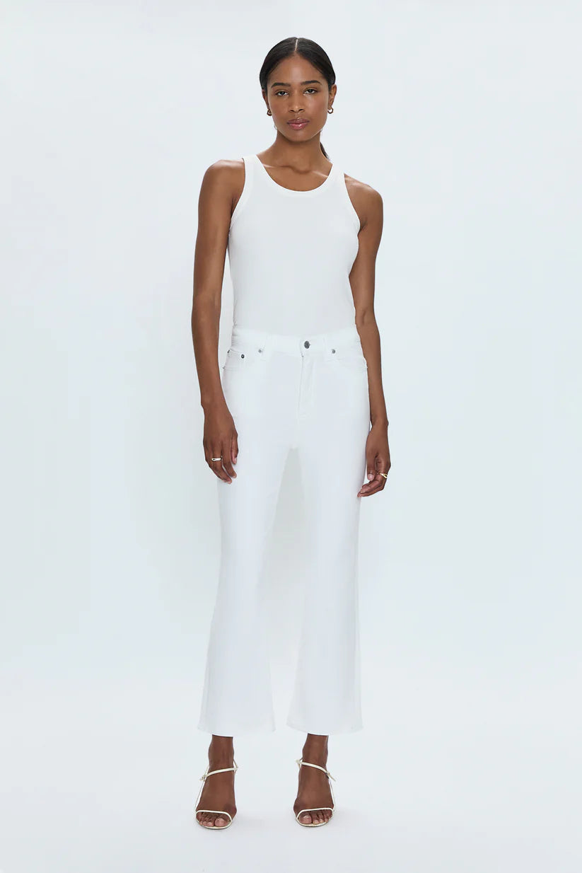 Woman wearing a white sleeveless top and white pants on a light gray background