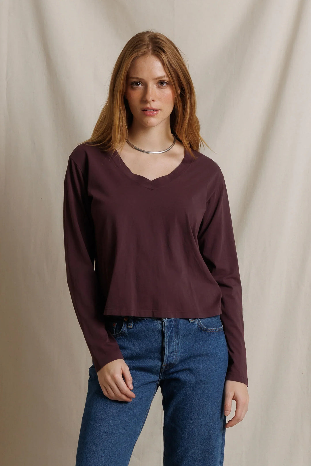 perfectwhitetee Jimi Cotton Long Sleeve Boxy V Neck Tee in Cherry Lacquer, front view on model, showing a deep oxblood long sleeve tee with wide V-neck and boxy cropped fit, styled with medium-wash jeans and a silver collar necklace