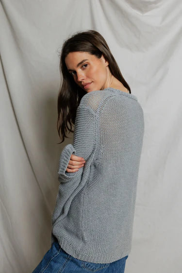 Model wearing Perfectwhitetee Margaret Cotton Slouchy Open-Knit Sweater in heather grey, styled with wide-leg blue denim, shown from the back at a three-quarter turn, against draped grey backdrop. - back