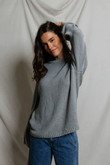 Model wearing Perfectwhitetee Margaret Cotton Slouchy Open-Knit Sweater in heather grey, styled with wide-leg blue denim, shown from the back at a three-quarter turn, against draped grey backdrop.