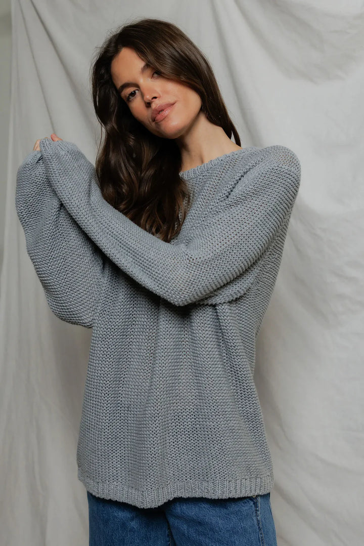 Model wearing Perfectwhitetee Margaret Cotton Slouchy Open-Knit Sweater in heather grey, styled with wide-leg blue denim, shown from the back at a three-quarter turn, against draped grey backdrop.