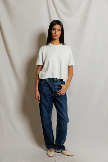 Woman wearing white cropped cotton knit cardigan buttoned at chest with crew neckline, styled with dark wash straight-leg denim and ivory ballet flats, neutral studio backdrop — perfectwhitetee Maude Cardigan
