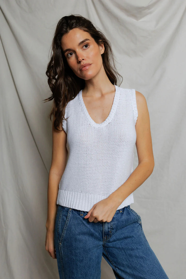 Woman wearing white open-stitch cotton knit tank with deep U-neckline and ribbed hem, styled with medium wash wide-leg denim and black slide sandals, neutral studio backdrop — perfectwhitetee Peggy Sweater Tank 2