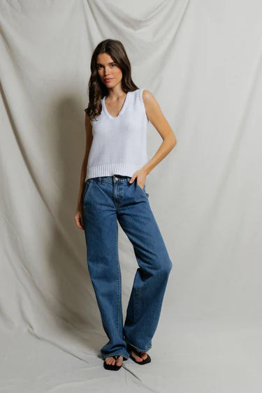 Woman wearing white open-stitch cotton knit tank with deep U-neckline and ribbed hem, styled with medium wash wide-leg denim and black slide sandals, neutral studio backdrop — perfectwhitetee Peggy Sweater Tank