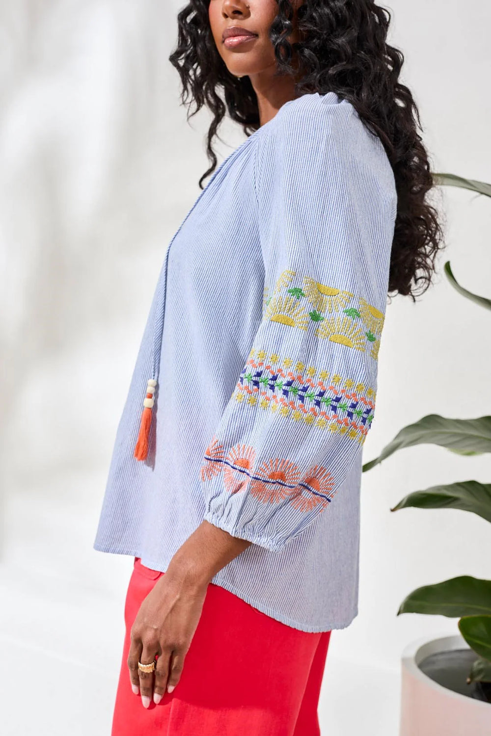 Close-up side view of Tribal Raglan Balloon Sleeve Blouse showing multicolor embroidery detail on balloon sleeve — yellow, coral, navy, and green floral and geometric stitching on blue yarn-dye stripe cotton.