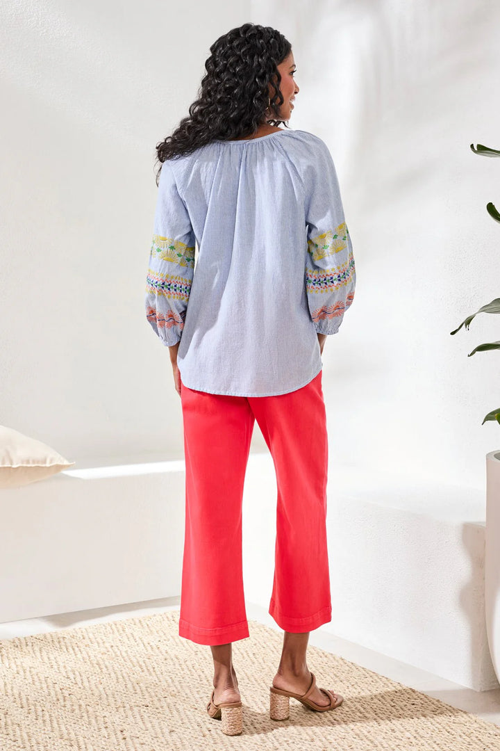 Back view of Tribal Raglan Balloon Sleeve Blouse in baja blue stripe, showing relaxed raglan silhouette and embroidered balloon sleeves with elasticized cuffs, styled with red wide-leg trousers.