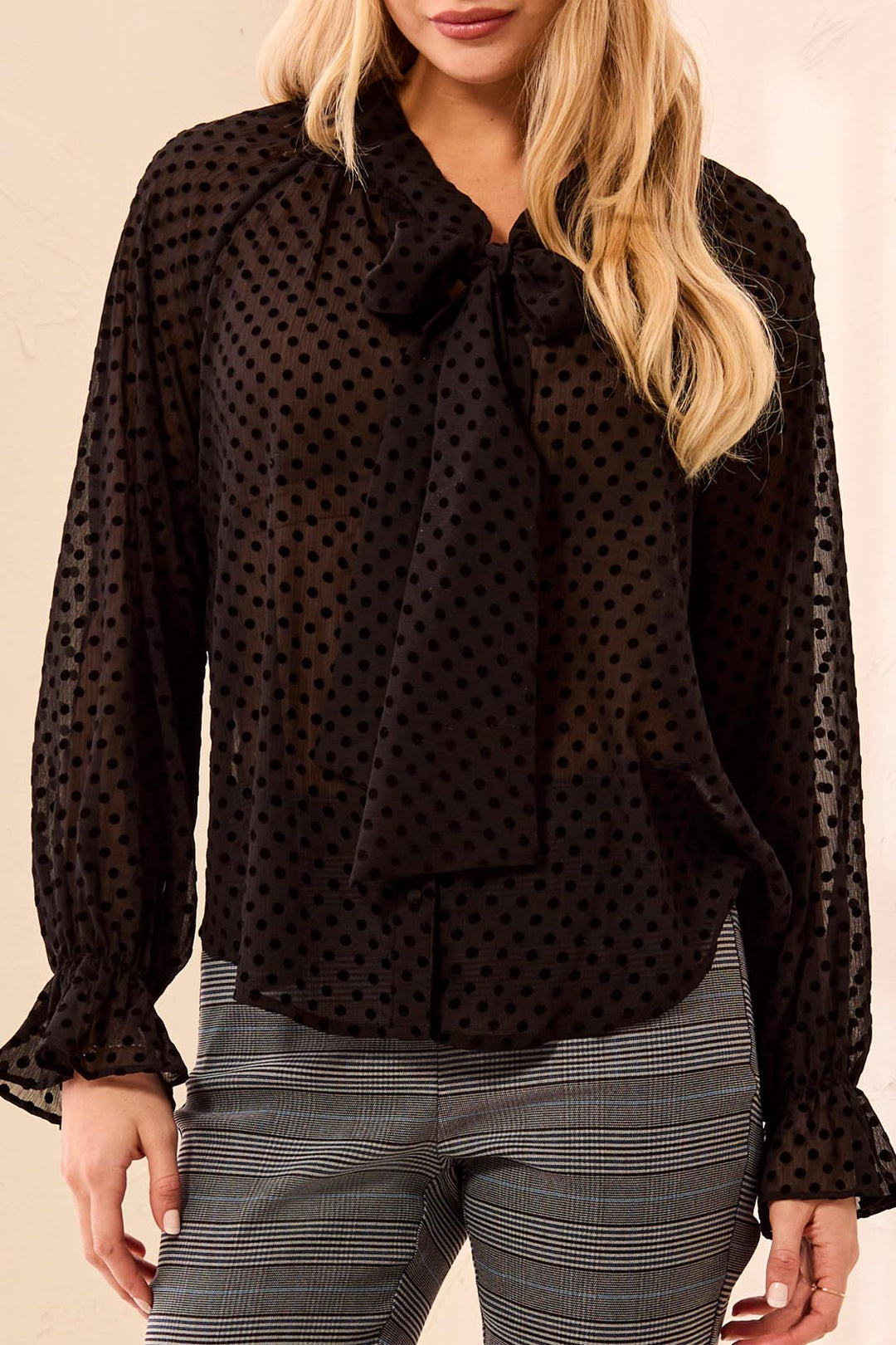 Tribal Long Sleeve Button Front Blouse with Tie in Black, front view on model, showing sheer flocked-dot chiffon, bow tie neckline, gathered shoulders, and ruffled cuffs, worn with glen plaid trousers.