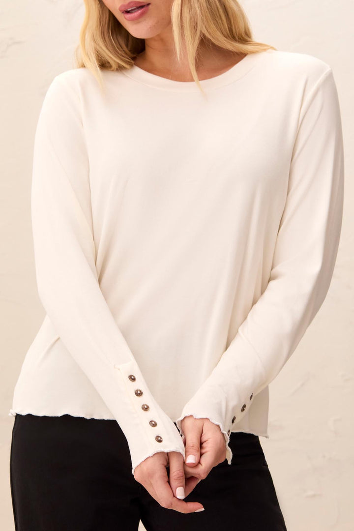 Tribal Long Sleeve Crew Neck Top with Button Detail in Moonstone, front view on model, showing banded crew neck, lettuce-edge hem, and extended sleeves with button-lined cuffs, worn with black pants.